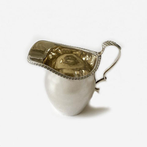 a silver cream jug with patterned edge and handle